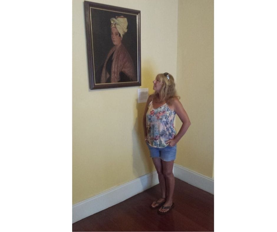 Janice Horton standing in front of a painting of Marie Laveau The Voodoo Queen of New Orleans 